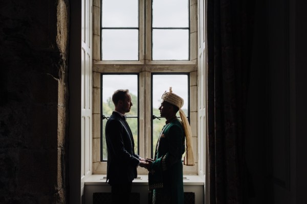 Silhouette of grooms standing at windowsill frame window