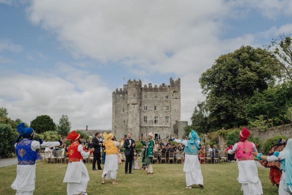 Grooms surrounded by guests and dancers castle in background