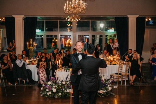 Grooms on dancefloor in dining room in front of guests