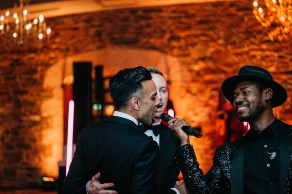 Grooms dance on dancefloor together singing into microphone