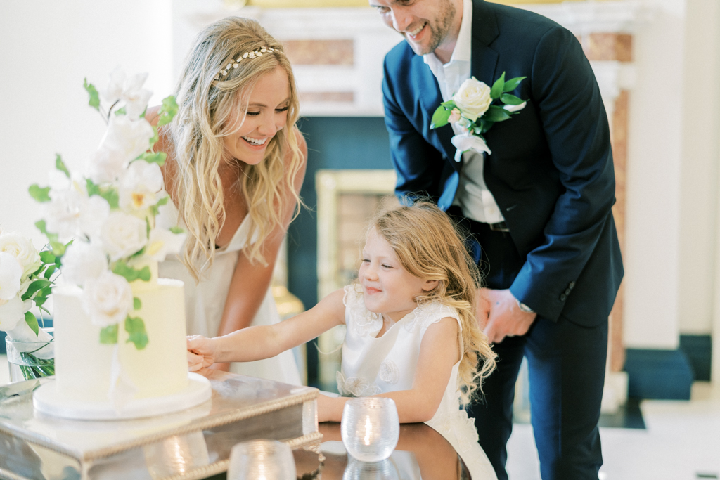 Bride little girl and groom cut the white wedding cake