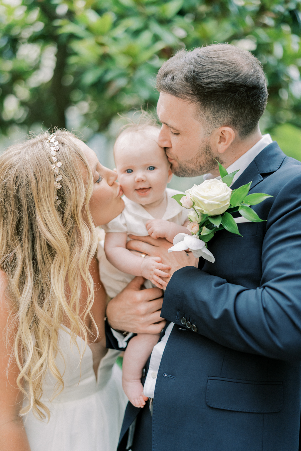 Bride and groom kiss little girl on the cheek she smiles