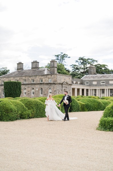 Bride and groom walking along pathway venue behind them