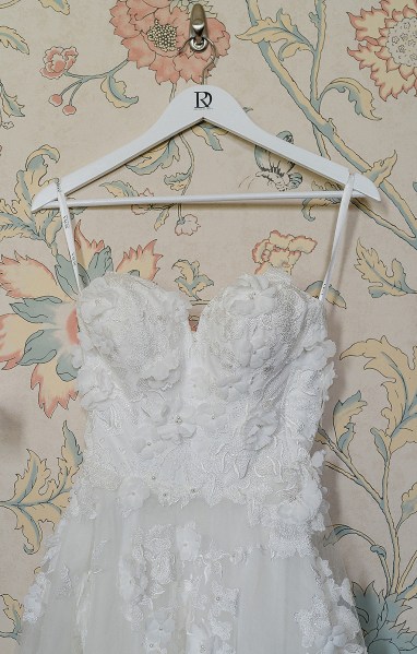 Wedding dress hanging in front of floral wallpaper in room