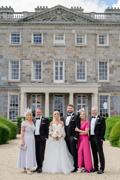 Mother daughter father groom family portrait bride pose for a photo in front of venue