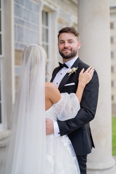 Bride and groom embrace veil from behind smiling