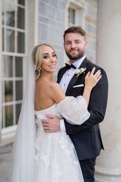 Bride and groom embrace veil from behind smiling