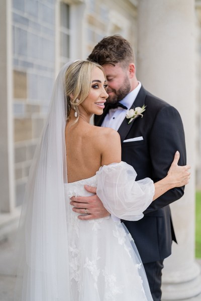 Bride and groom embrace veil from behind smiling