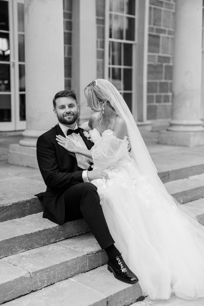 Bride and groom sitting on steps to wedding venue pillars black and white