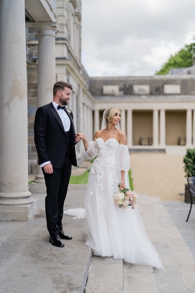 Bride and groom standing on steps to wedding venue pillars