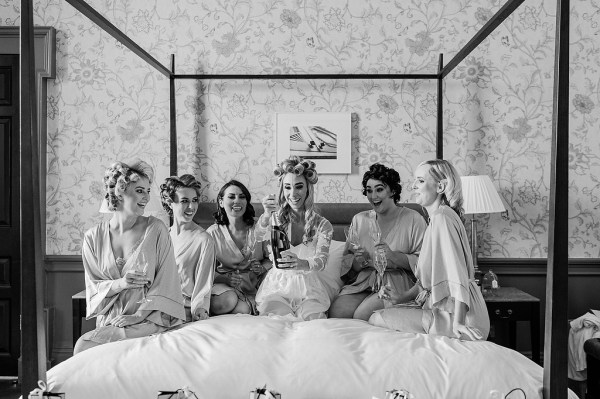 Black and white image of bride and bridesmaids sitting on the bed opening gifts