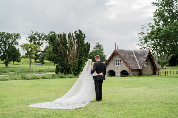 Bride and groom walking on grass away from camera they hug and embrace