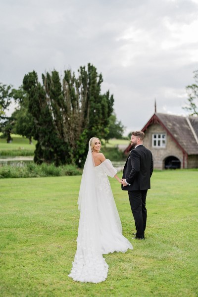 Bride and groom walking on grass away from camera bride looks over her shoulder