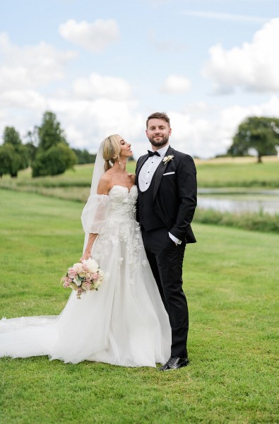 Bride and groom walk downhill on grass lake in background