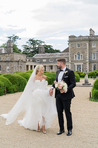 Bride and groom walk along pathway to wedding venue castle