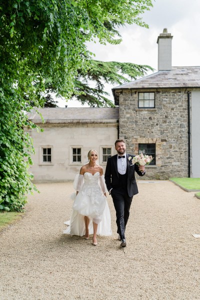 Bride and groom walk along pathway to wedding venue castle