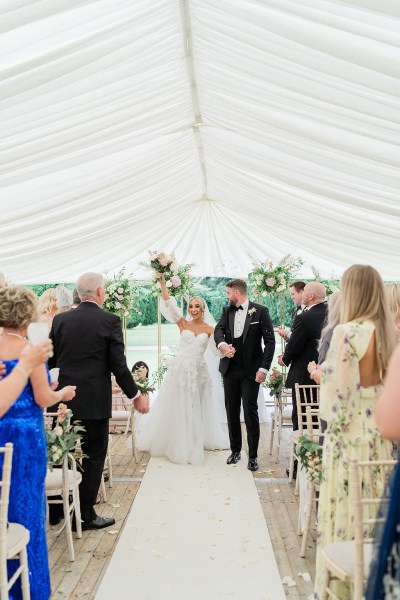 Confetti thrown on couple bride and groom exit ceremonial room guests clap bouquet in the air