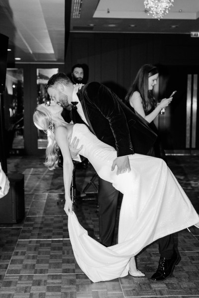 Black and white image of groom leaning bride over kissing her