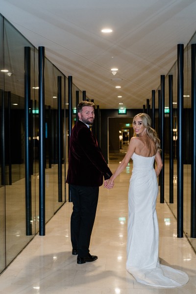 Bride looks over her shoulder hand in hand holding hands with groom