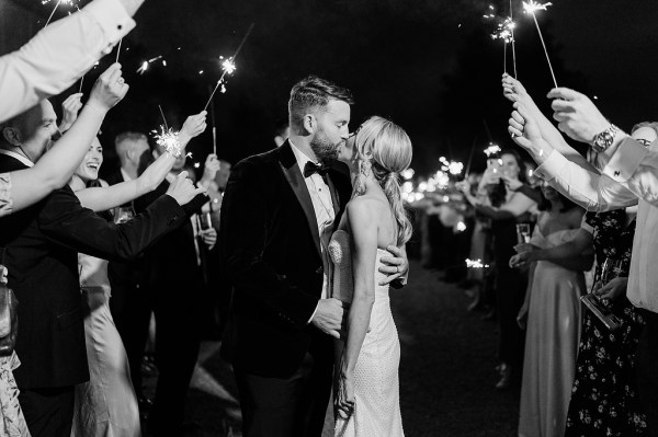 Black and white image of bride and groom kissing guests have sparklers over their heads