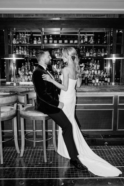 Bride leans on groom at bar in pub stools black and white