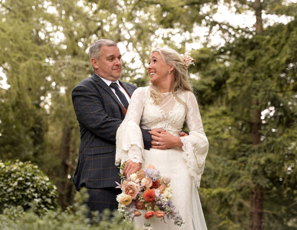 OC Wedding Videography: Lisa & Ian couple hugging each other in forest groom bride holding bouquet flowers