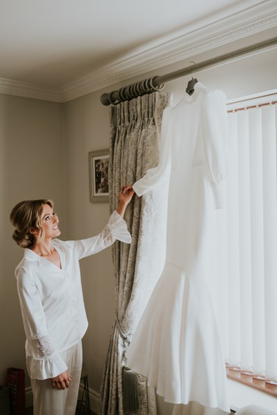 Bride holding bridal gown/dress at window