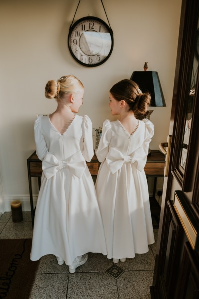 Two little girls wearing white dresses bow on back