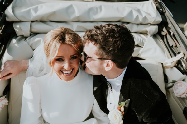 Groom kissing brides cheek in wedding car