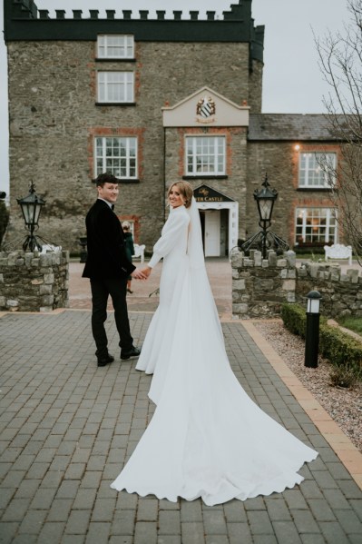 Bride and groom look over their shoulders walking towards wedding venue