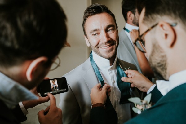 Groomsman smiles as man takes picture of him blue tie