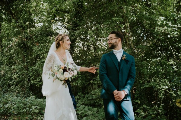 Bride follows groom in forest and she holds bouquet flowers