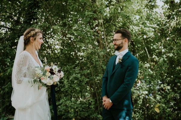 Bride follows groom in forest and she holds bouquet flowers