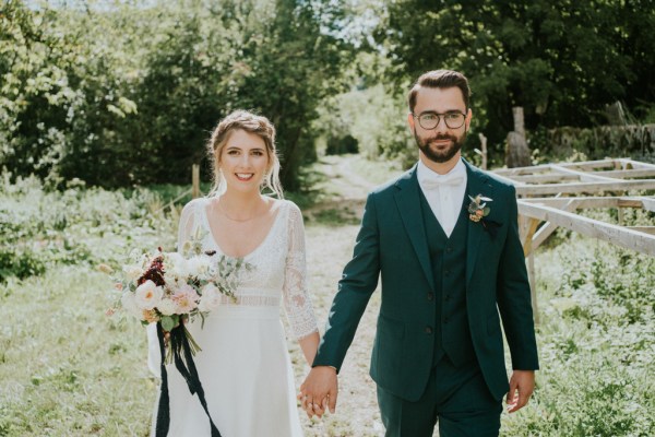 Bride and groom hand in hand along pathway to forest/park