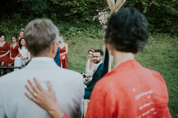 Bride and groom look towards man and woman wearing suit and orange