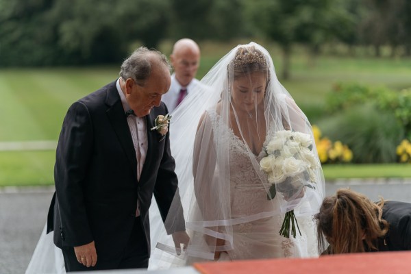 Father of the bride helps her up the steps to church