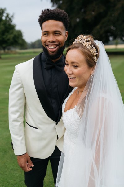 Bride and groom stand on grass smiling