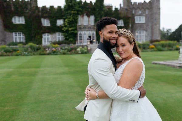 Bride and groom embrace on the grass in front of wedding venue