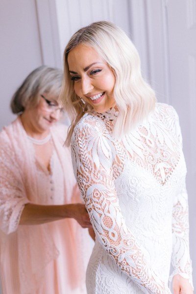 Mother helps zip back of brides dress bride laughs and smiles