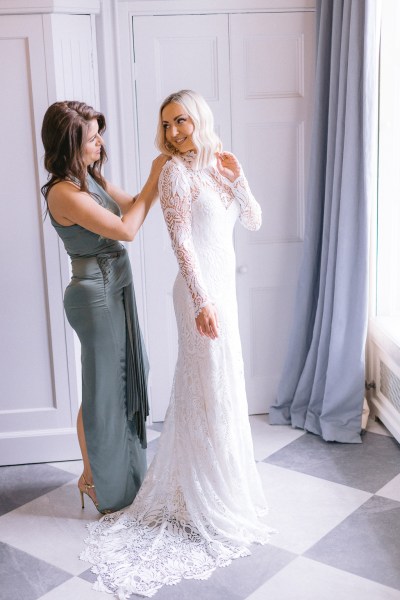 Bridesmaid helps with brides hair and dress