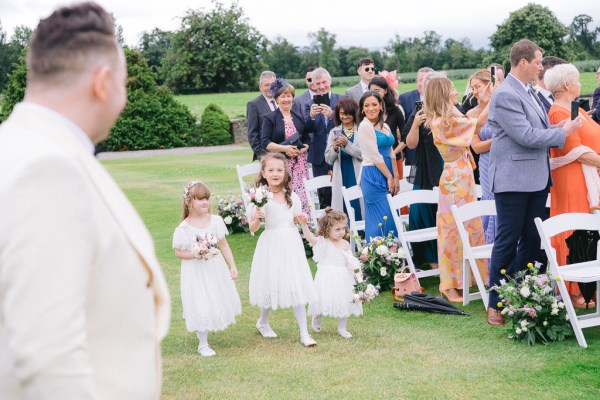 Three little flower girls walk the grass aisle