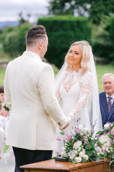 Emotional bride looks at groom during ceremony holding hands