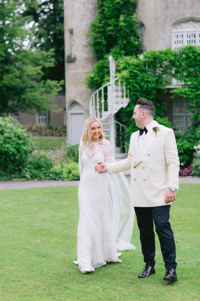 Bride and groom stand in garden on the grass together staircase behind them