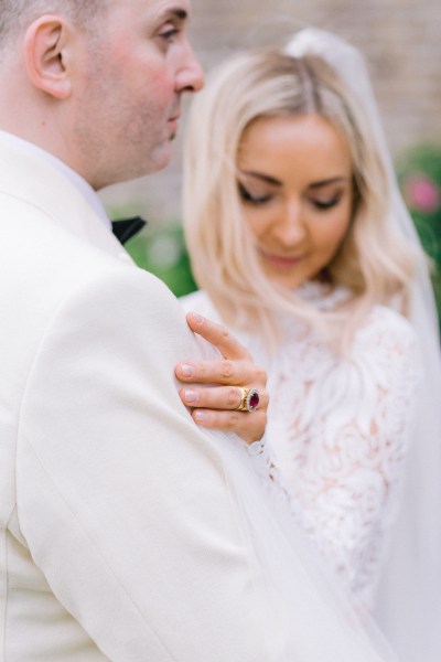 Bride shows off wedding hand band/ring looks down groom hugs her