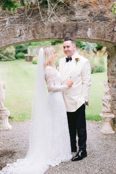 Bride and groom stand in garden under archway