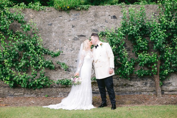 Bride and groom kiss in front of walled garden ivy