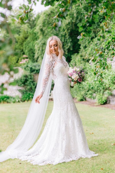 Bride standing in garden holding bouquet flowers wall