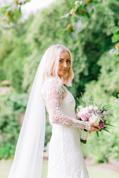 Bride standing in garden holding bouquet flowers wall