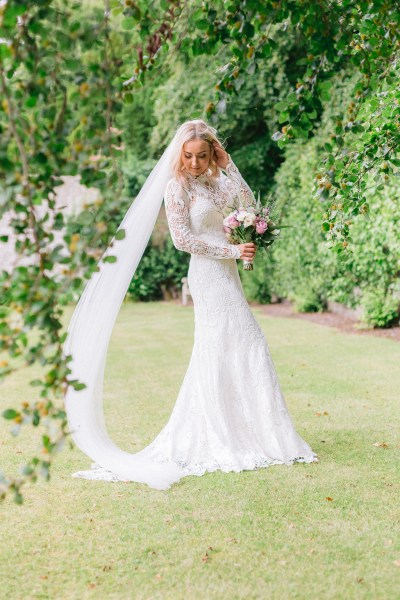 Bride standing in garden holding bouquet flowers wall