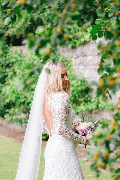 Bride standing in garden holding bouquet flowers wall